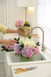 Photo of Woman making bouquet with beautiful hydrangea flowers in kitchen, closeup