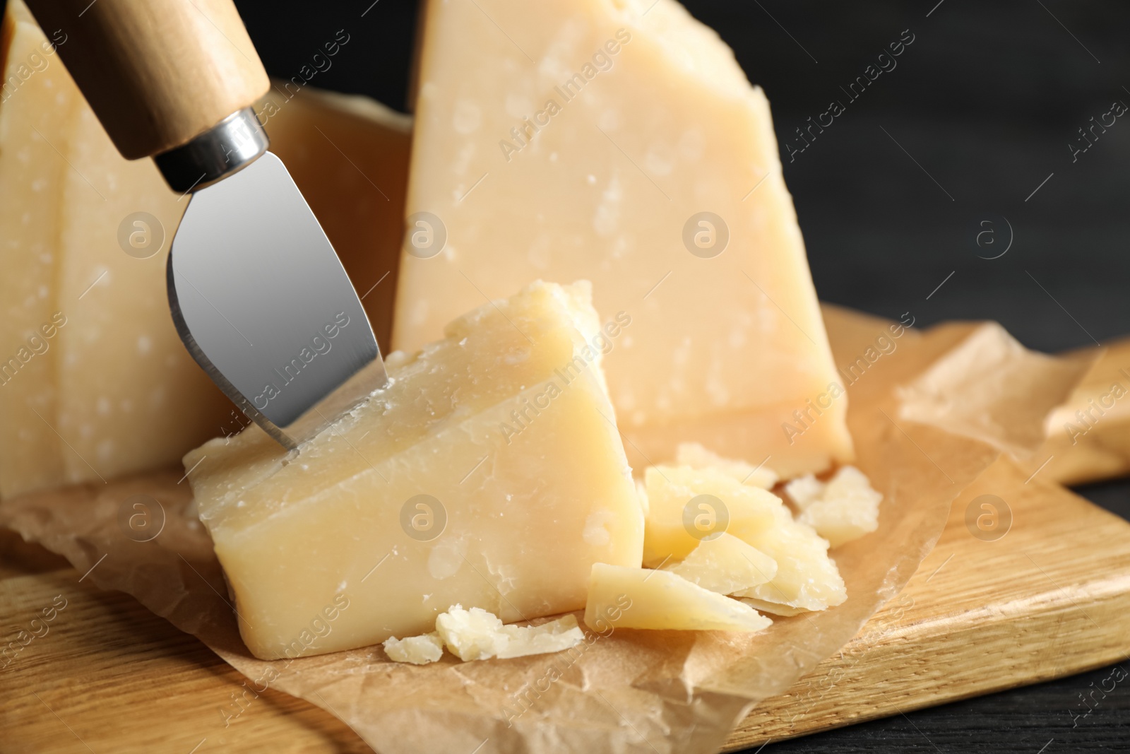 Photo of Pieces of Parmesan cheese and knife on wooden board, closeup