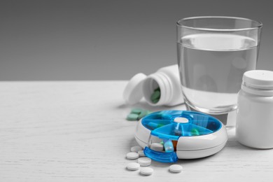 Photo of Pill box with medicaments and glass of water on white wooden table. Space for text