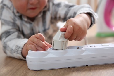 Little child playing with power strip and plug on floor indoors, closeup. Dangerous situation