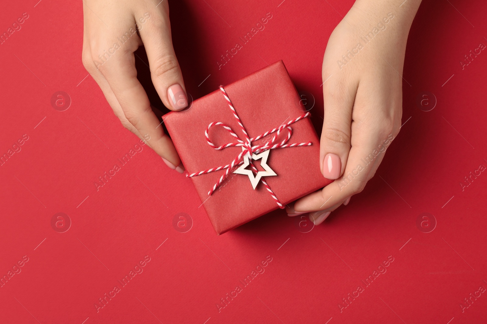 Photo of Christmas present. Woman with beautifully wrapped gift box on red background, top view