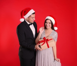 Photo of Man presenting Christmas gift to his girlfriend on red background