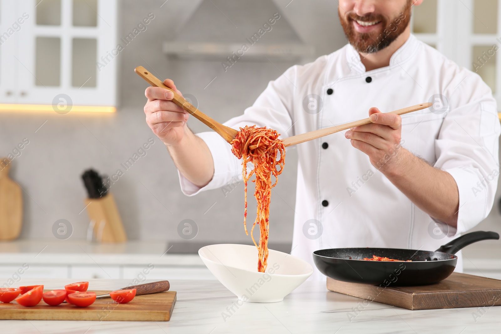 Photo of Professional chef putting delicious spaghetti into bowl at marble table in kitchen, closeup