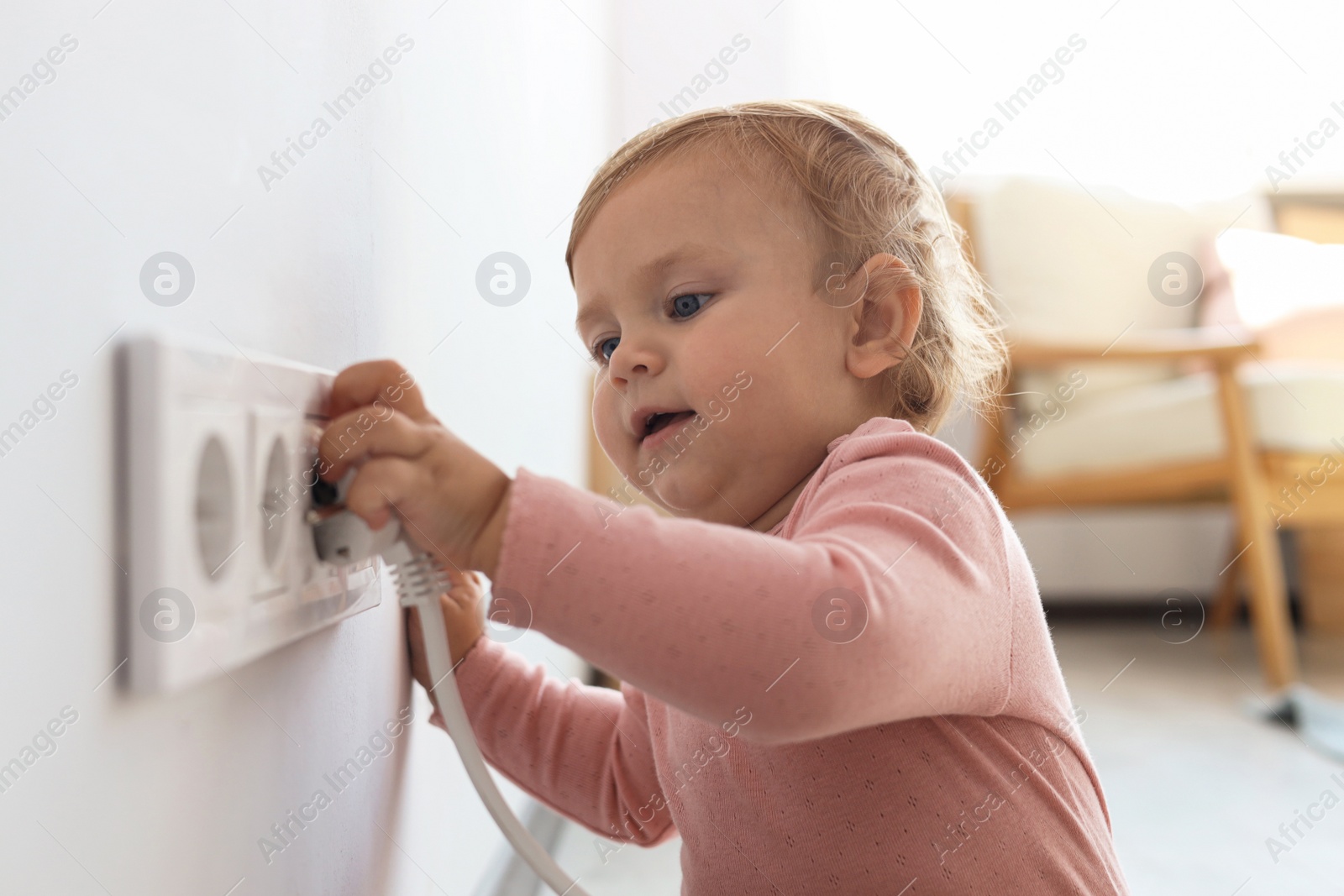 Photo of Cute baby playing with electrical socket and plug at home. Dangerous situation