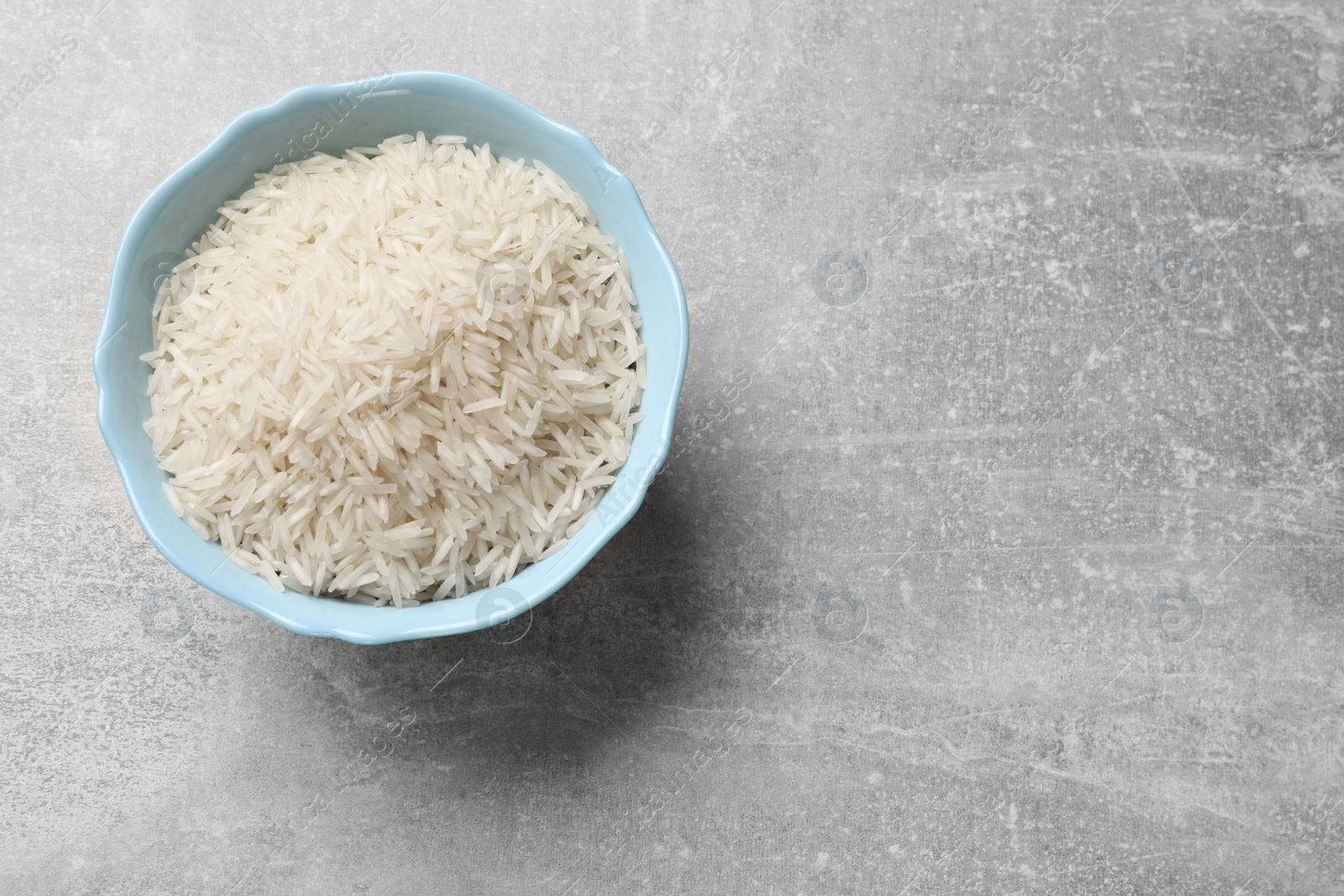 Photo of Raw basmati rice in bowl on grey table, top view. Space for text