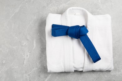 Photo of Blue karate belt and white kimono on gray marble background, top view. Space for text