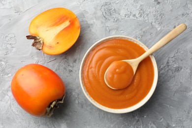 Photo of Delicious persimmon jam and fresh fruits on grey table, flat lay