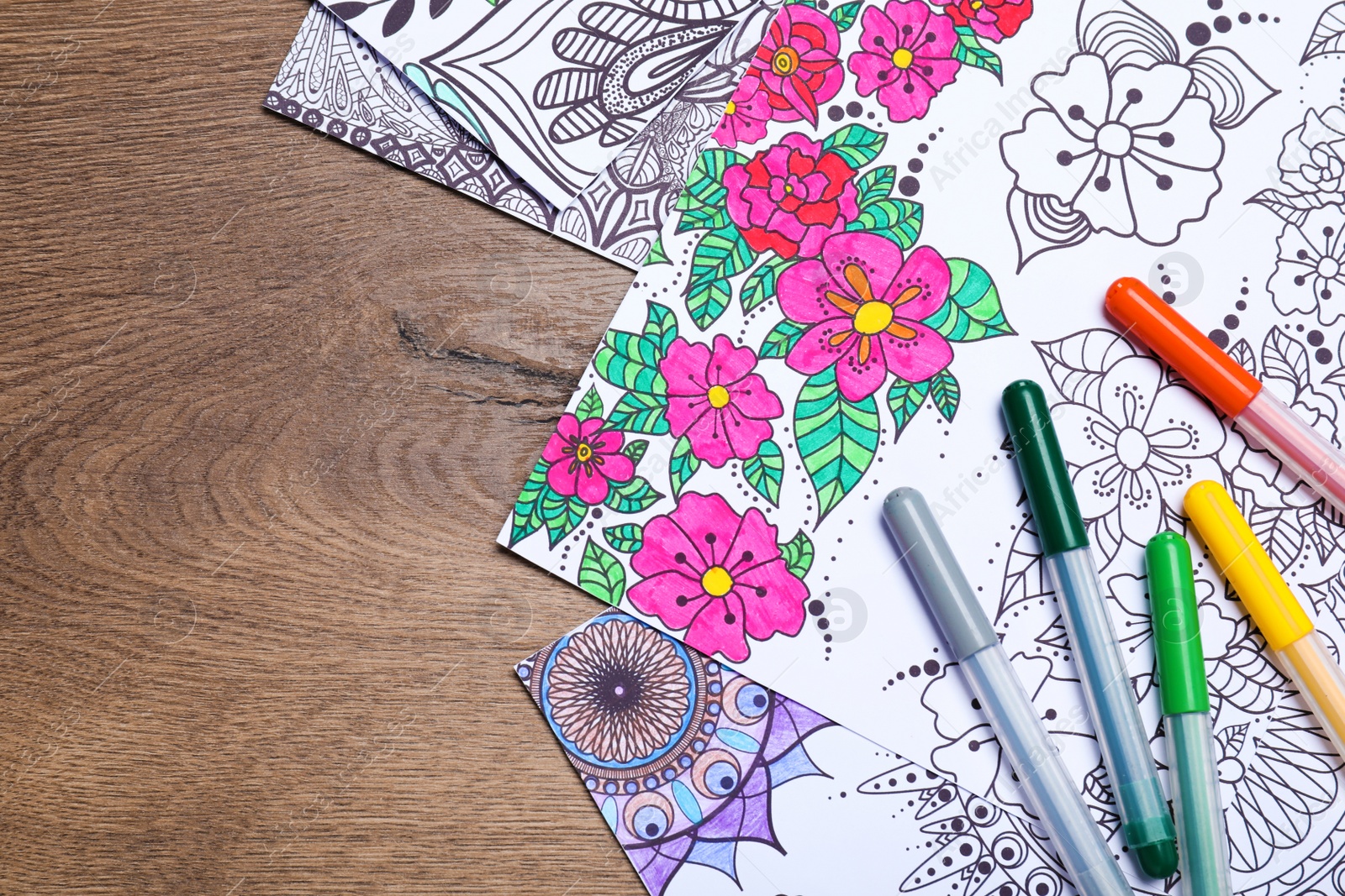 Photo of Antistress coloring pages and felt tip pens on wooden table, flat lay. Space for text