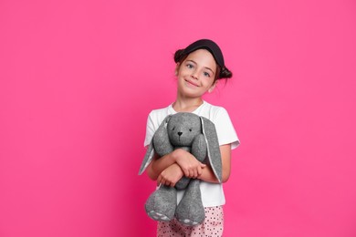 Cute girl in pajamas with sleep mask and toy bunny on pink background