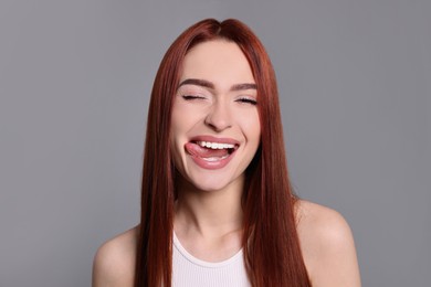 Photo of Happy woman with red dyed hair showing tongue on light gray background