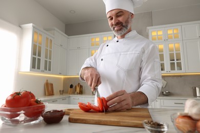 Photo of Professional chef cutting tomatoes at white marble table indoors, low angle view