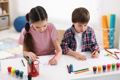 Happy brother and sister drawing at white table in room