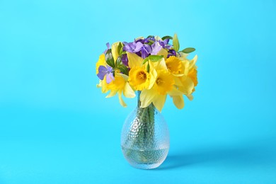 Photo of Bouquet of beautiful yellow daffodils, iris and periwinkle flowers in vase on light blue background