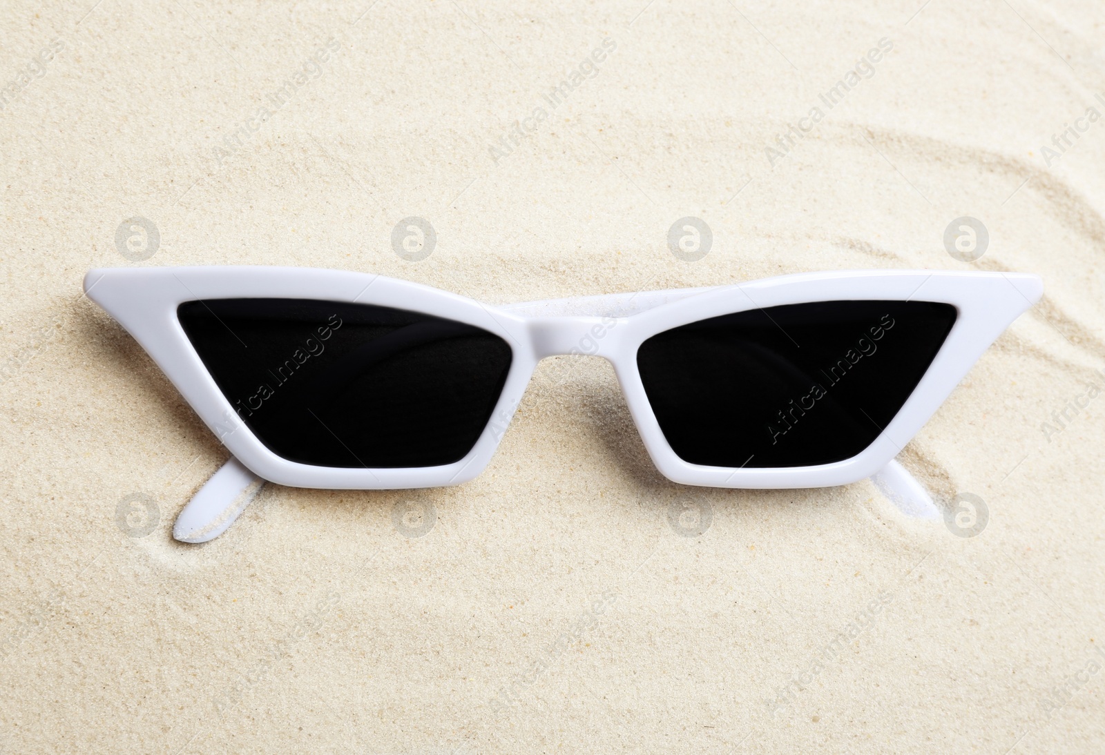 Photo of Stylish sunglasses on white sand. Summer time