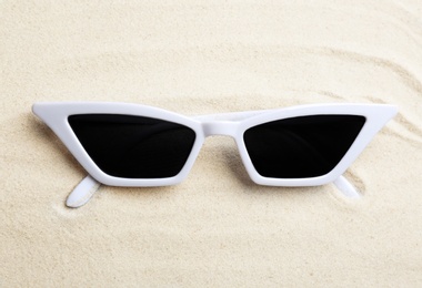 Stylish sunglasses on white sand. Summer time