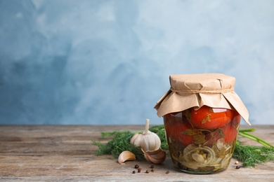 Pickled tomatoes in glass jar and products on wooden table against blue background, space for text