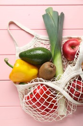 Photo of String bag with different vegetables and fruits on pink wooden table, top view