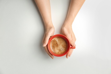 Young woman with cup of delicious hot coffee on light background, top view