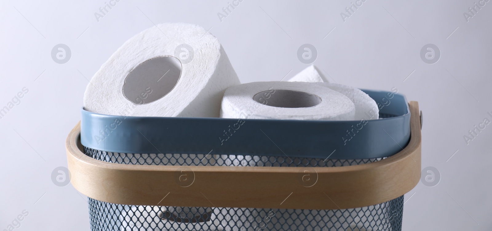 Photo of Toilet paper rolls in basket against light grey wall, closeup. Banner design