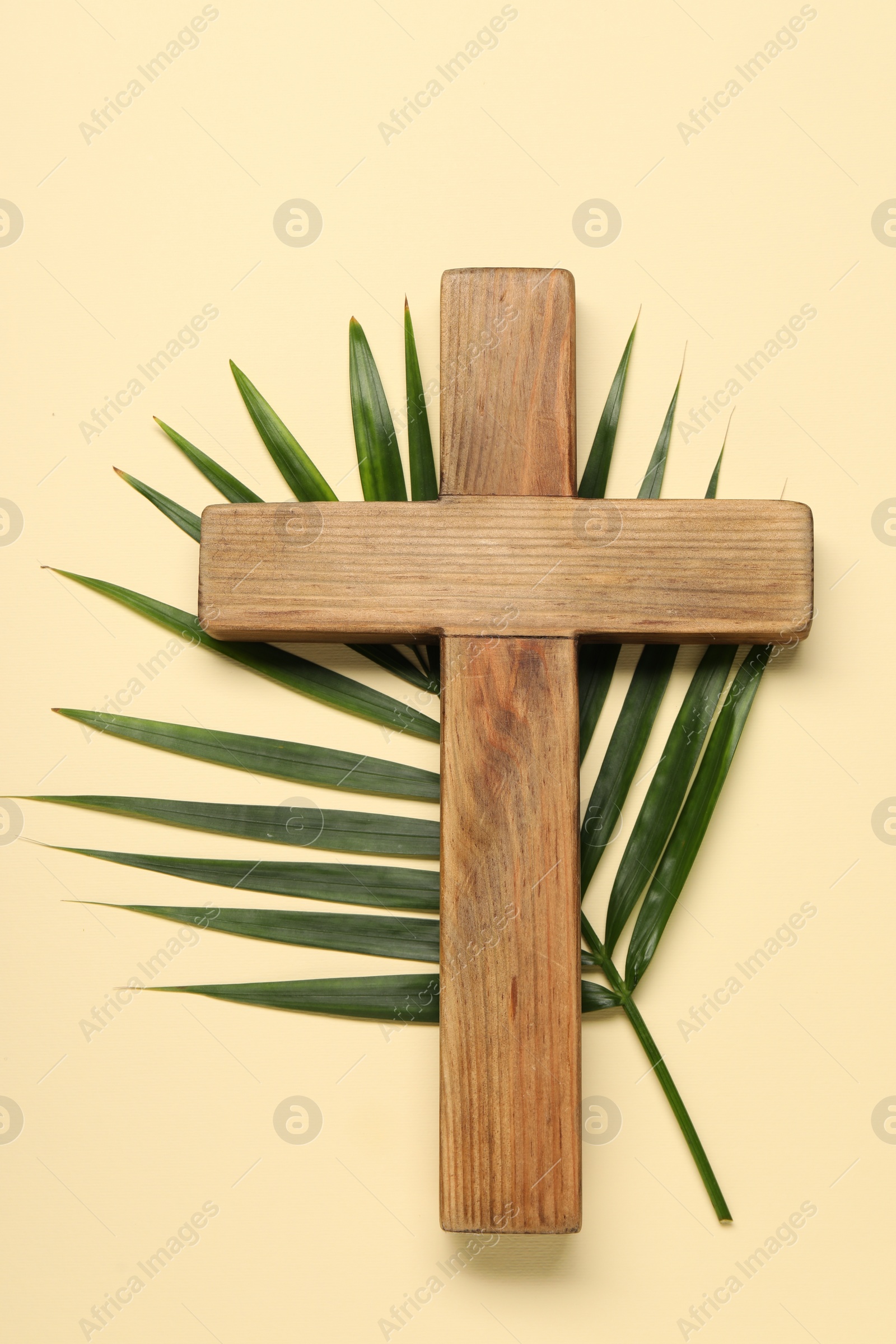 Photo of Wooden cross and palm leaf on beige background, top view. Easter attributes