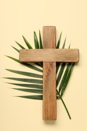 Wooden cross and palm leaf on beige background, top view. Easter attributes