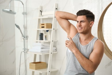 Photo of Handsome man applying deodorant to armpit in bathroom, space for text