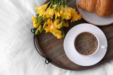 Photo of Morning coffee, croissant and flowers on bed, top view. Space for text