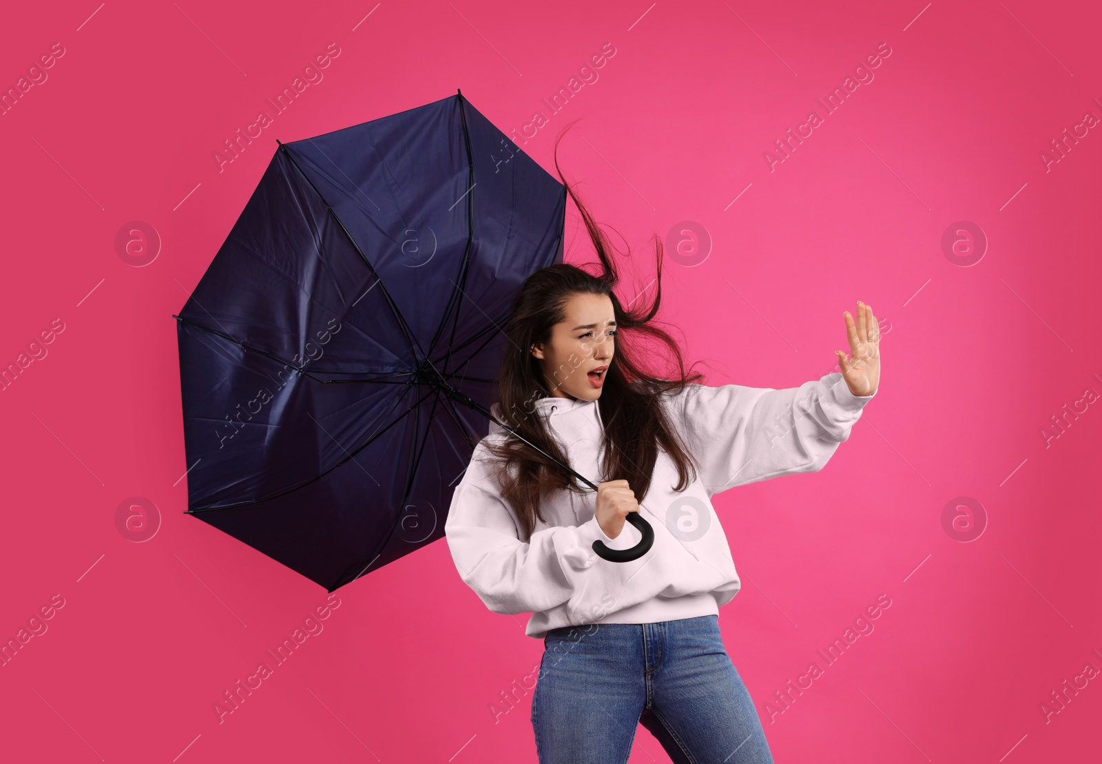 Photo of Emotional woman with umbrella caught in gust of wind on pink background