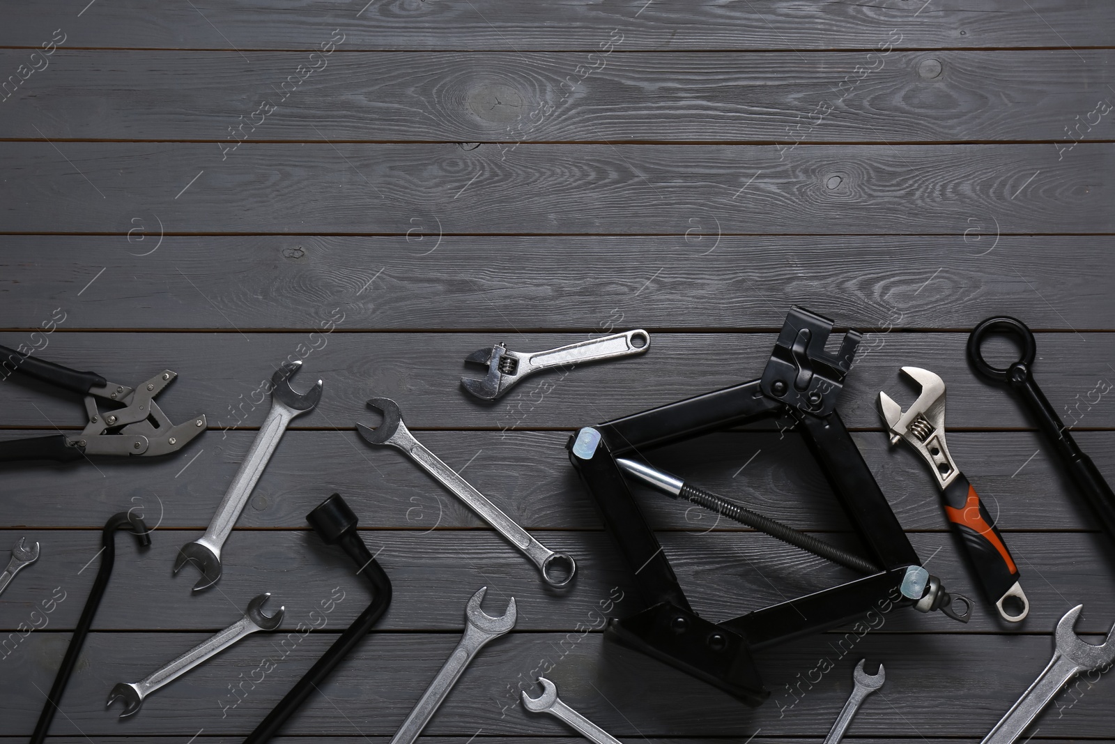 Photo of Car scissor jack and different tools on grey wooden surface, flat lay. Space for text