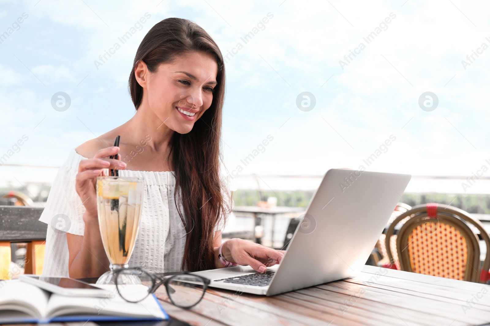 Photo of Beautiful woman with laptop and refreshing drink at outdoor cafe