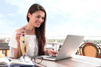 Photo of Beautiful woman with laptop and refreshing drink at outdoor cafe
