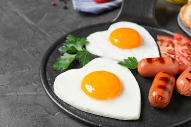 Photo of Delicious breakfast with heart shaped fried eggs and sausages on dark grey table, closeup