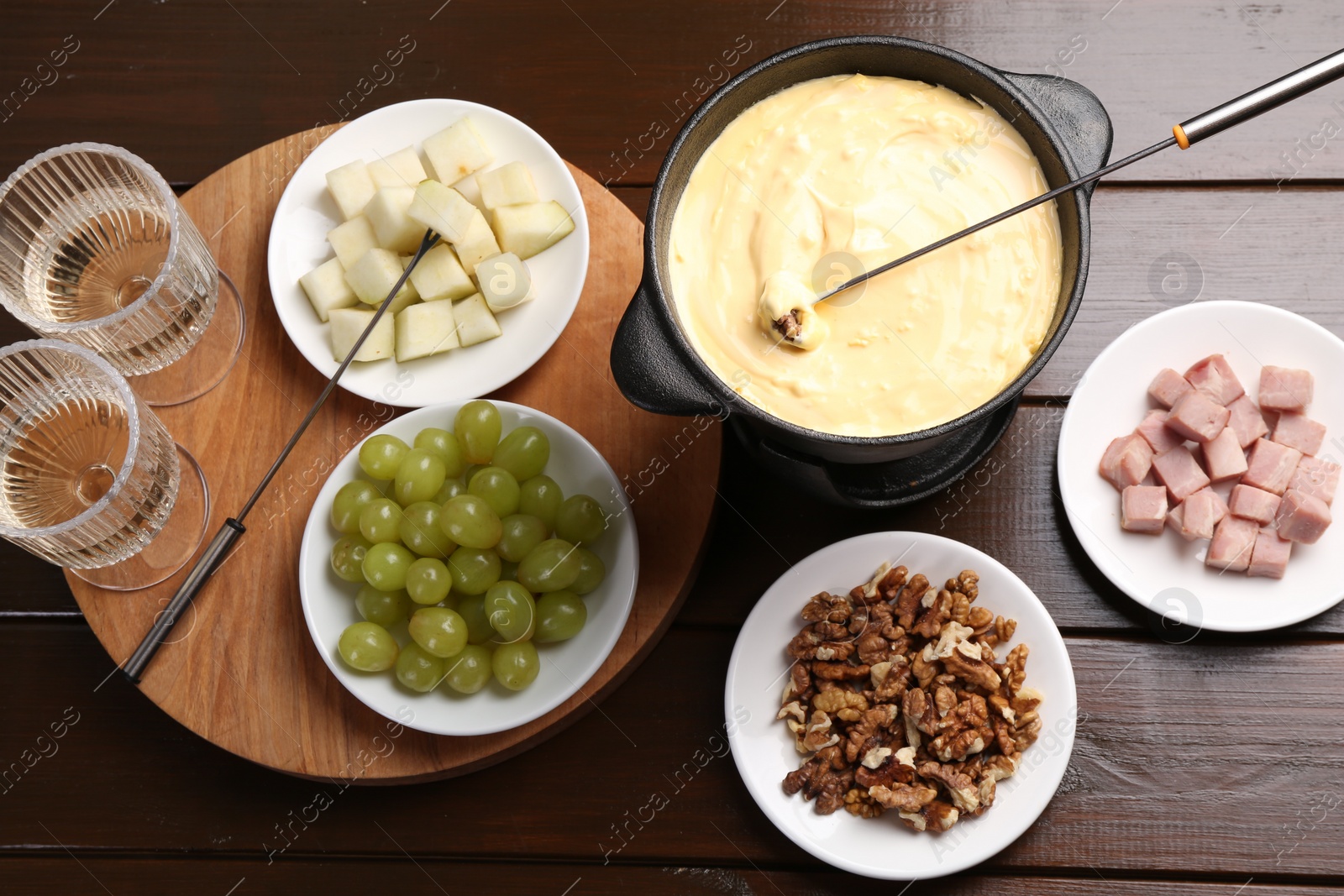 Photo of Fondue pot with tasty melted cheese, forks, wine and different snacks on wooden table, flat lay