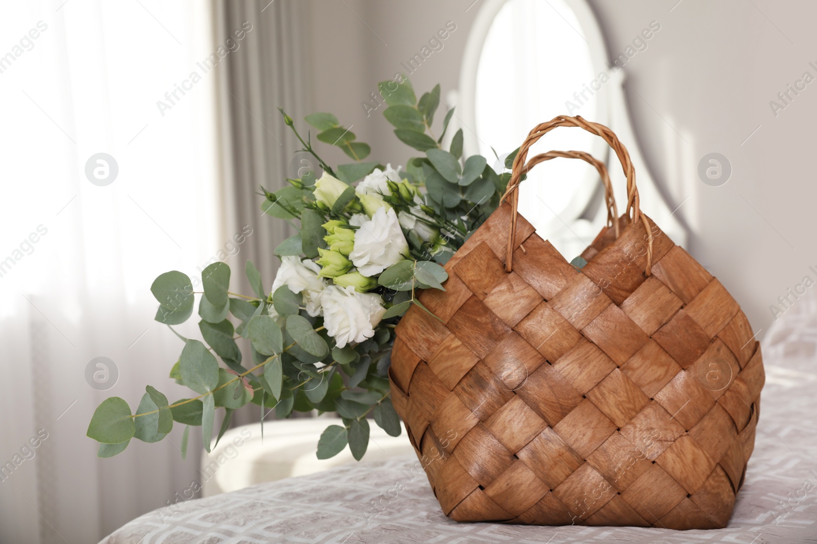 Photo of Stylish wicker basket with bouquet on bed indoors