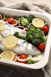 Photo of Raw fish with vegetables and lemon in baking dish on wooden table