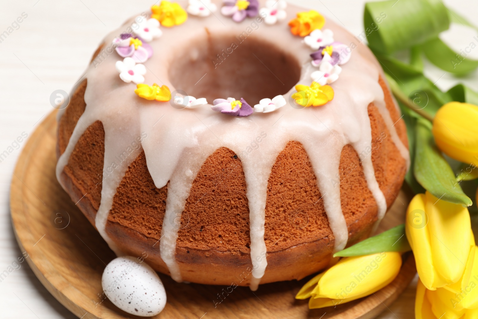 Photo of Delicious Easter cake decorated with sprinkles near egg and beautiful tulips on white wooden table, closeup