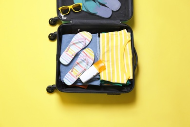 Photo of Open suitcase and beach accessories on yellow background, top view
