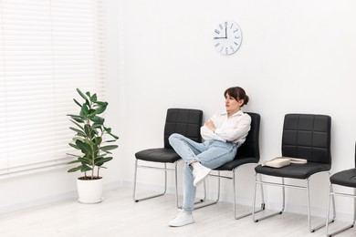 Photo of Woman sitting on chair and waiting for appointment indoors