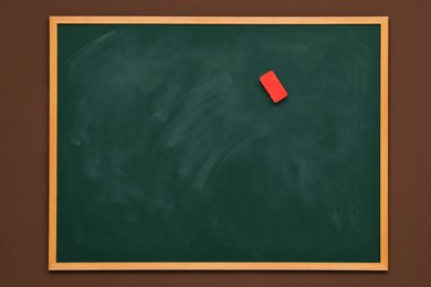 Photo of Dirty green chalkboard with duster hanging on brown wall
