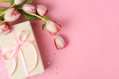 Photo of Beautiful gift box with bow, tulips and confetti on pink background, flat lay. Space for text