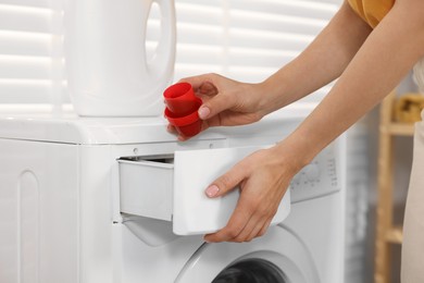 Woman with laundry detergent near washing machine indoors, closeup