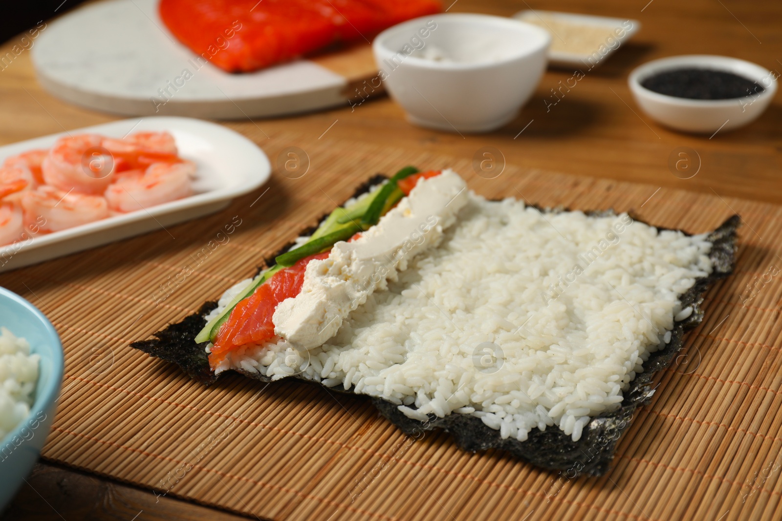 Photo of Unwrapped sushi roll with rice, cucumber, cheese and salmon on wooden table, closeup