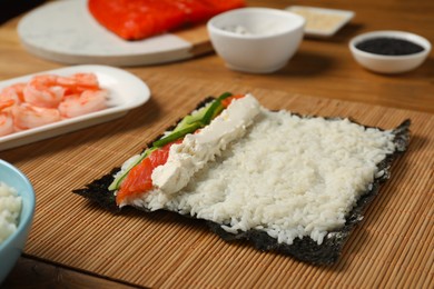 Unwrapped sushi roll with rice, cucumber, cheese and salmon on wooden table, closeup