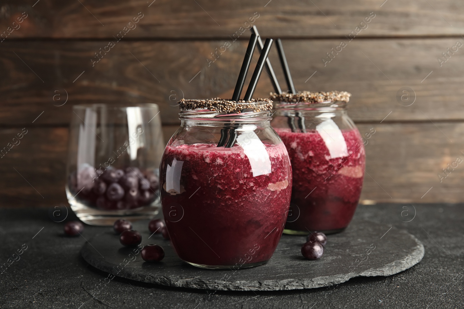 Photo of Jars of delicious acai juice with cocktail straws on dark table against wooden background