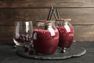 Photo of Jars of delicious acai juice with cocktail straws on dark table against wooden background