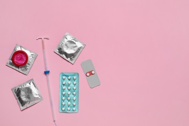 Photo of Contraception choice. Pills, condoms and intrauterine device on pink background, flat lay. Space for text