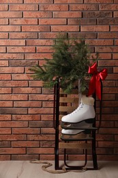 Photo of Sleigh with pair of ice skates and fir branches near brick wall indoors
