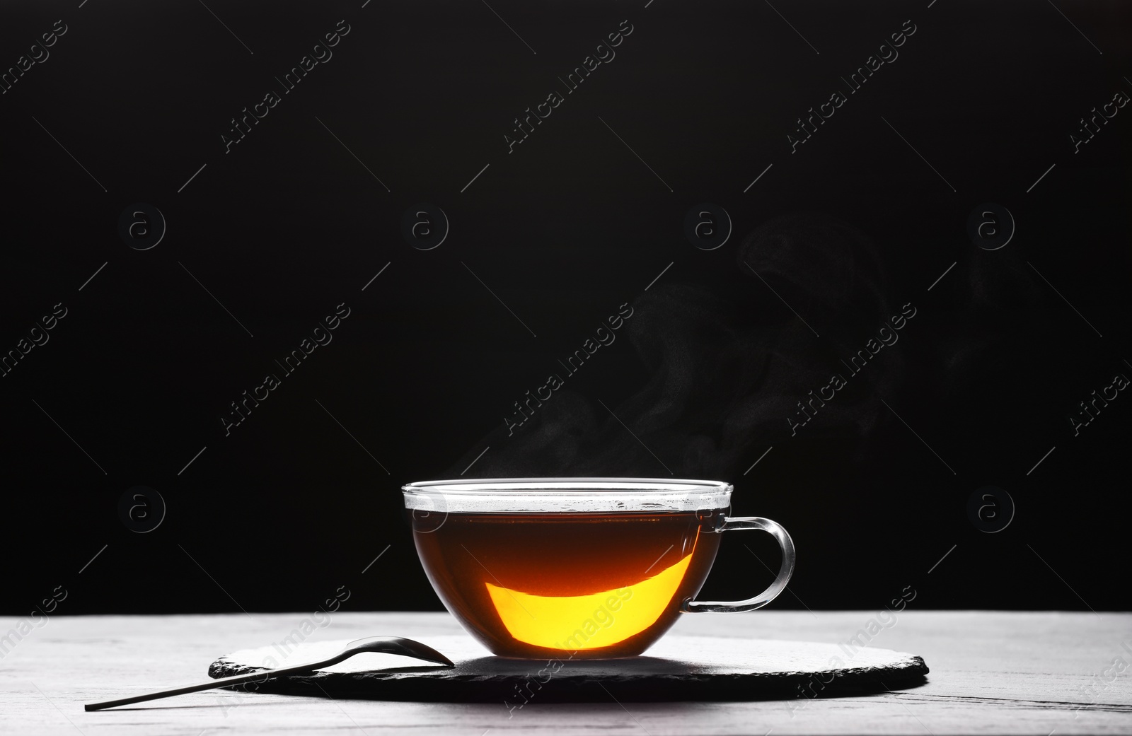 Photo of Glass cup of tea on table against black background, space for text