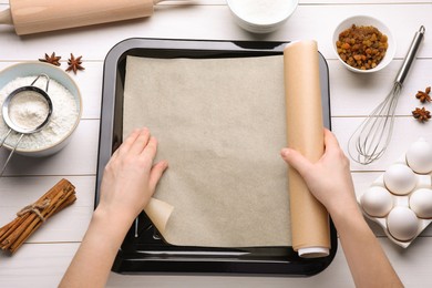 Woman putting parchment paper into baking pan over white wooden table, flat lay