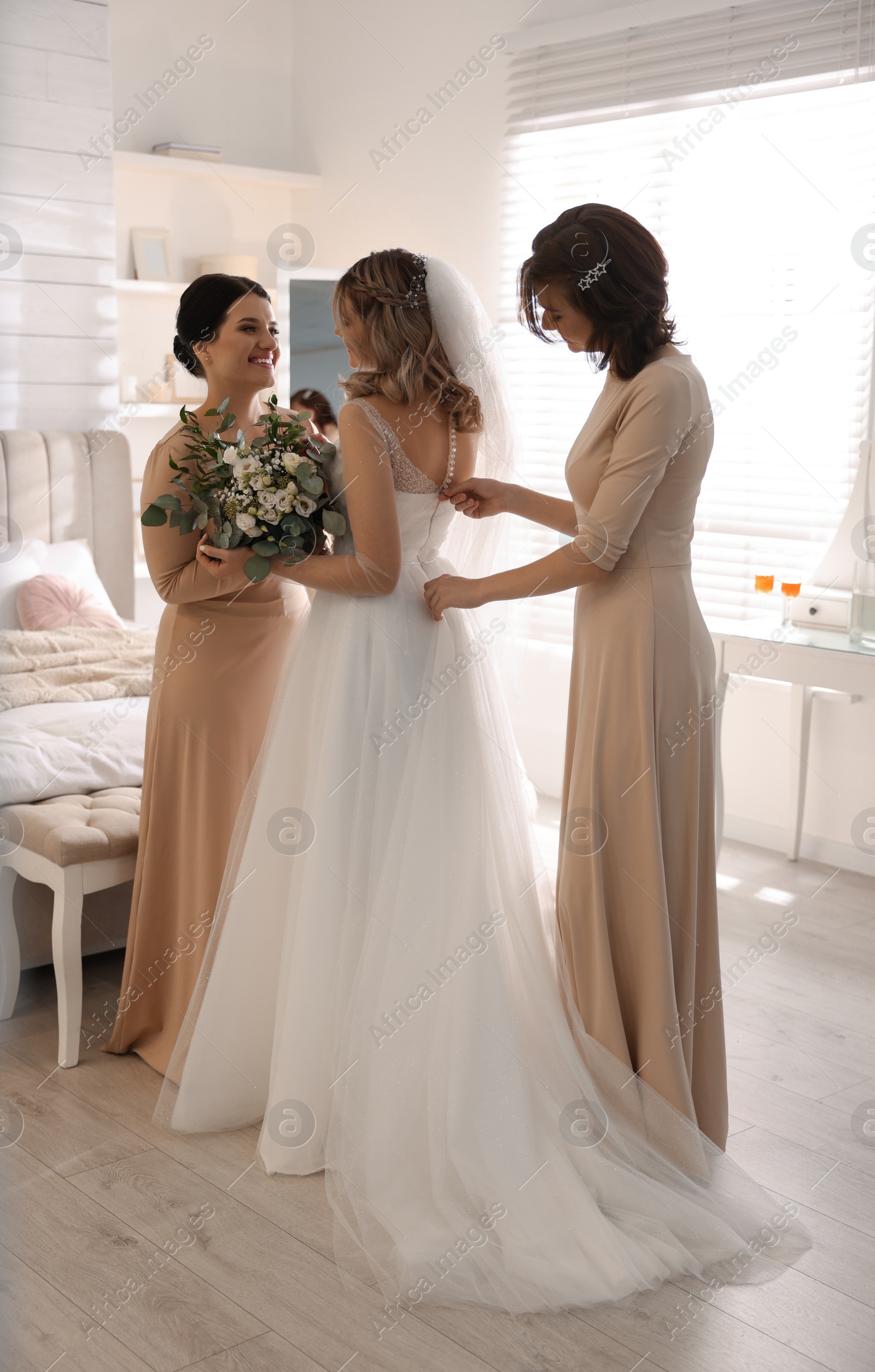 Photo of Happy bride with bouquet and bridesmaids in room at home. Wedding day